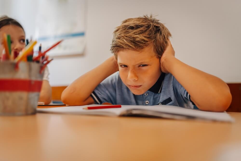 frustrierter Volksschüler, dem es zu laut in der Klasse ist 
