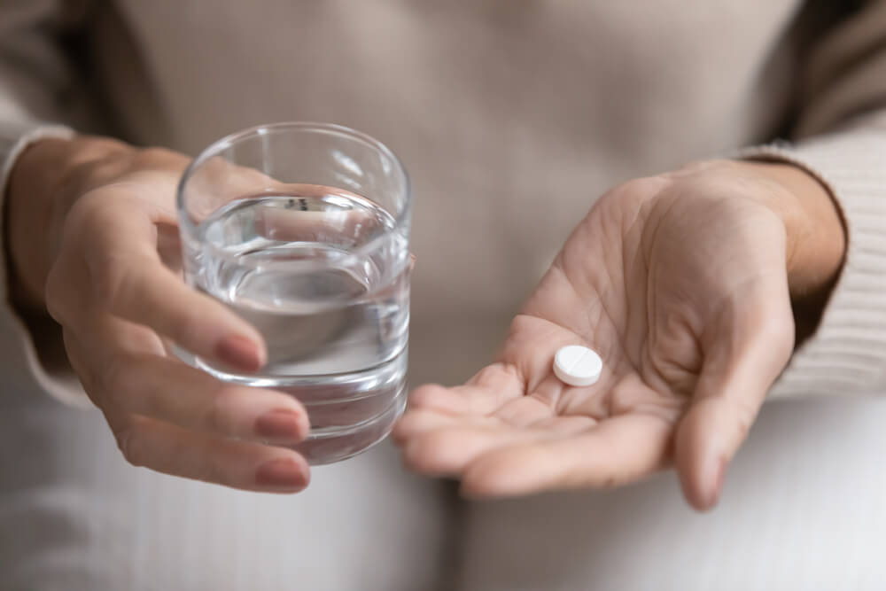Acetylsalicylsäure - Frau nimmt eine Tablette mit einem Glas Wasser