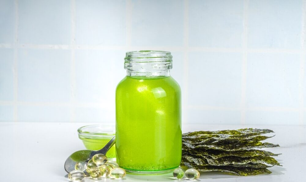 Algenöl: Glas mit grünen Algenöl und Kapseln mit Omega-3-Fettsäure
