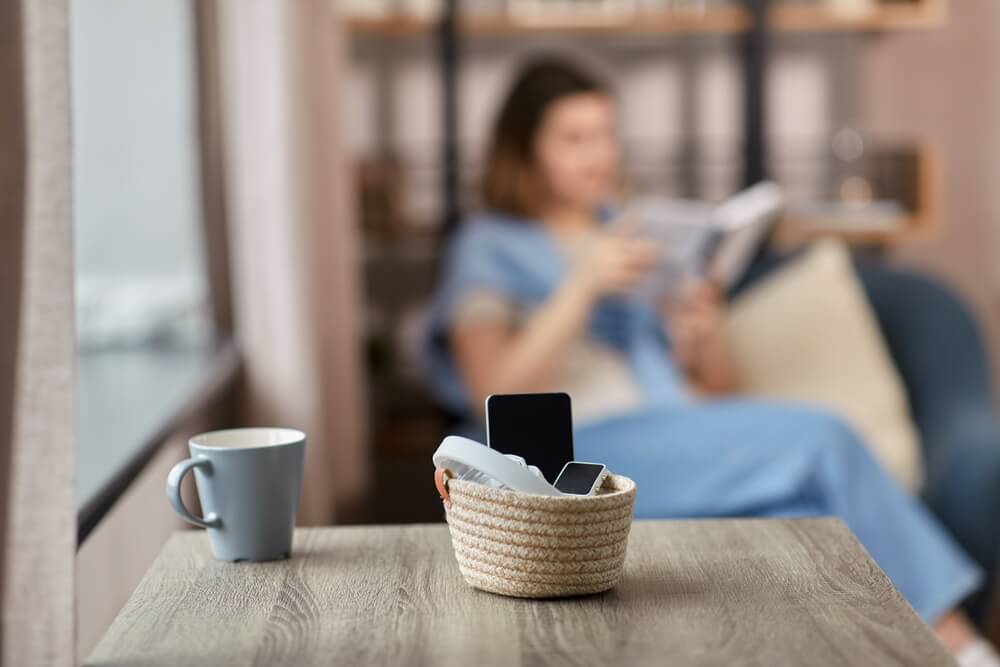 Digital Detox: Frau liest ein Buch und Smartphone ist in einem Korb weit weg