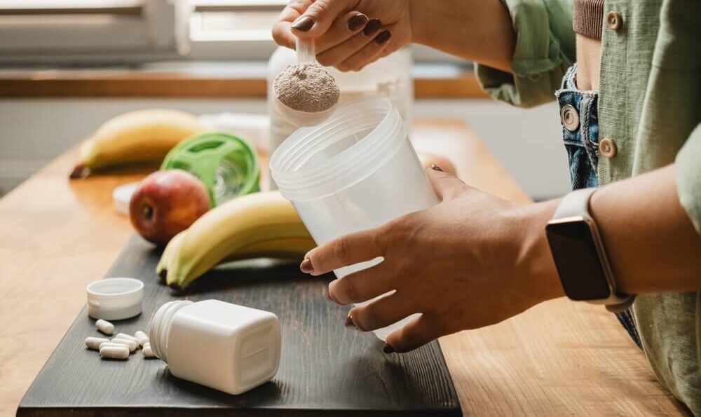 Frau mit Kreatin-Pulver in der Küche. Mit Obst beim Shake vorbereiten