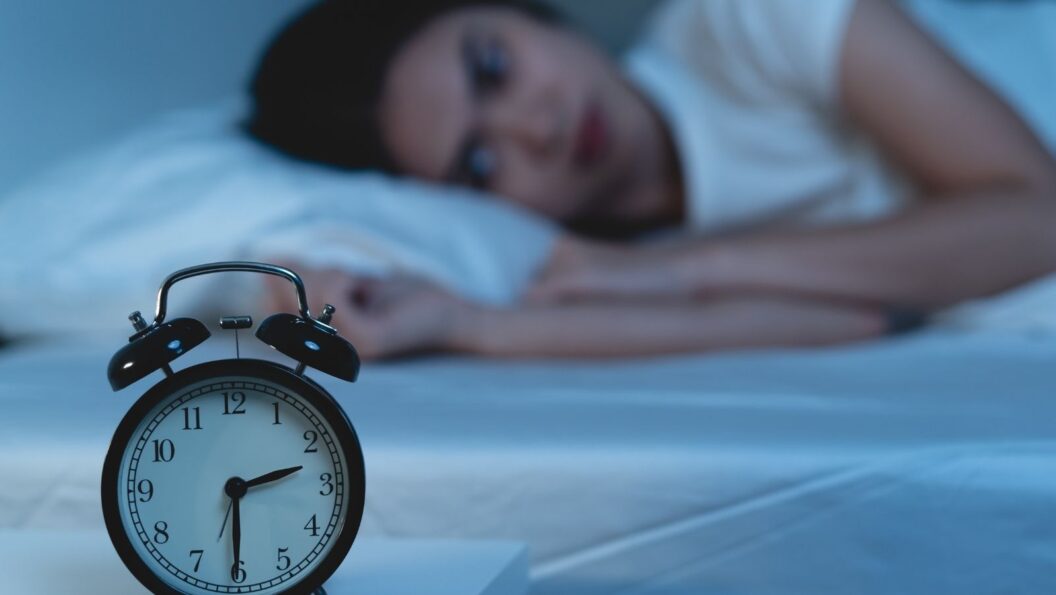 Schlaflosigkeit: schlaflose Frau mit Uhr in der Nacht im Bett