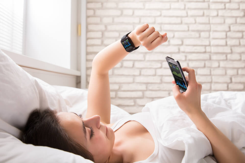 Frau, die ihren Schlaf mit Smartwatch und Smartphone trackt